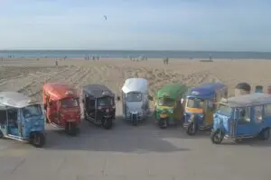 Seven colourful tuk tuks lined up on the beach at Scheveningen, ready for a fun ride