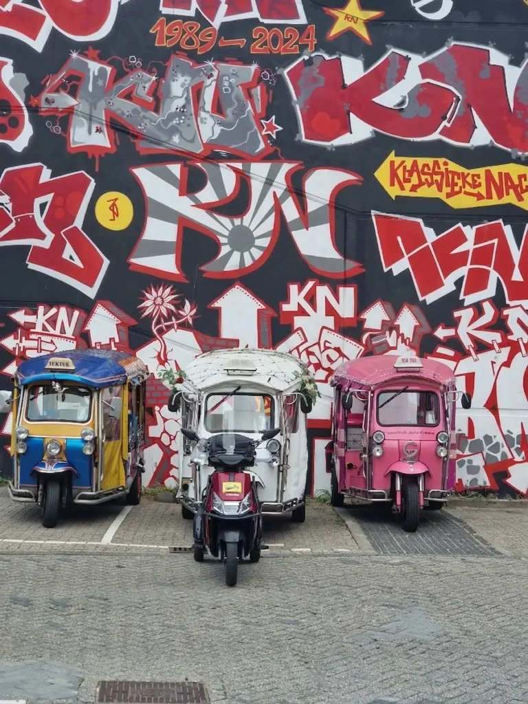 Startplaats in Den Haag met een blauwe, witte en roze Tuk Tuk, vergezeld door de nieuwe rode Tukkie scooter