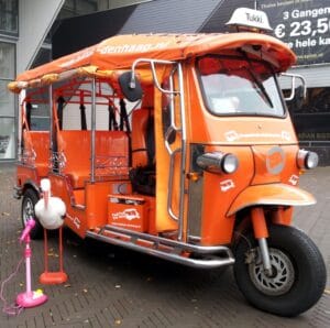 Orange tuk tuk of Tuk Tuk The Hague with a stork statue in front