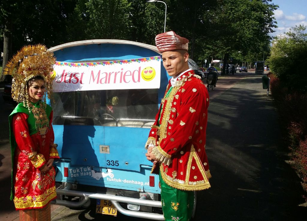 Bride and groom in traditional Indonesian dress next to a tuk tuk with a Just Married banner