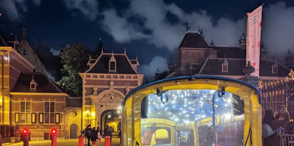 Gelbes Tuk-Tuk mit Lichterkette vor dem beleuchteten Stadhouderspoort-Tor des Binnenhofs in Den Haag am Abend
