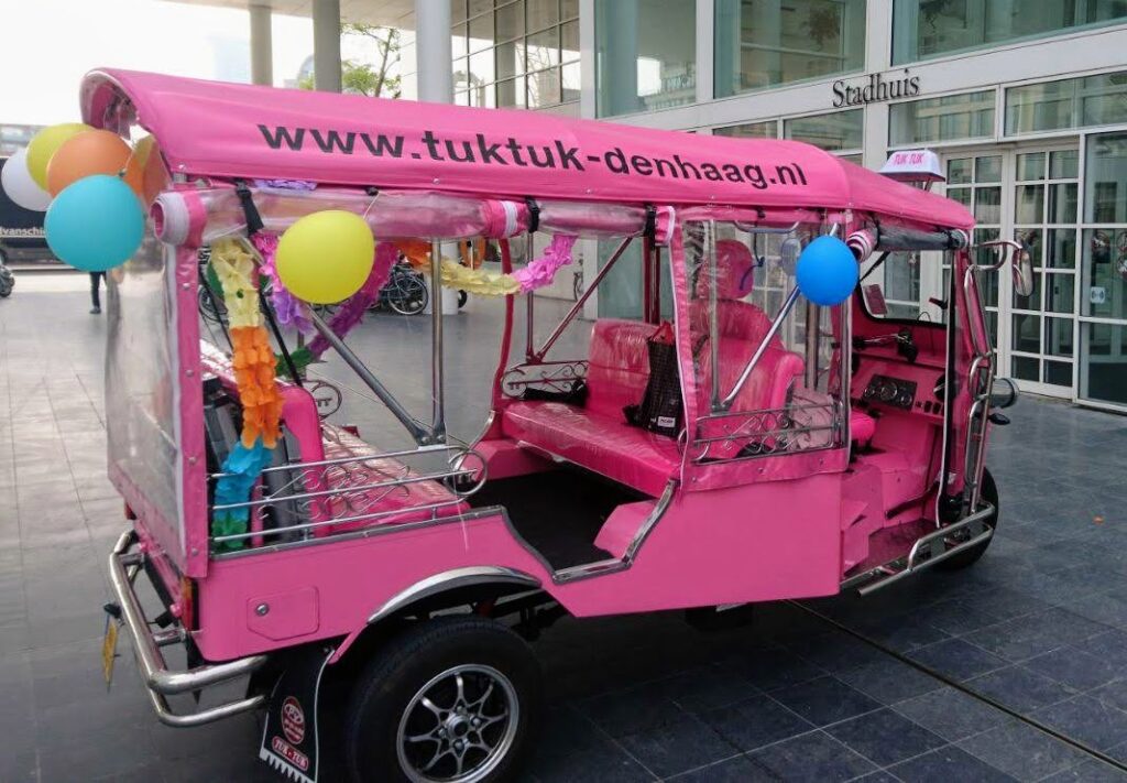 Pink wedding tuk tuk with balloons in front of The Hague City Hall, where the couple gets married