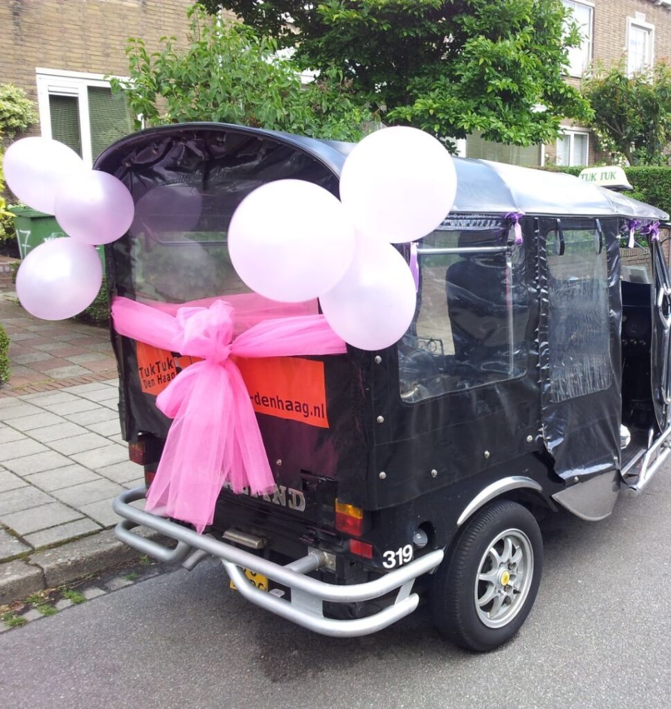 Black tuk tuk decorated with pink balloons and a bow as wedding transport in The Hague