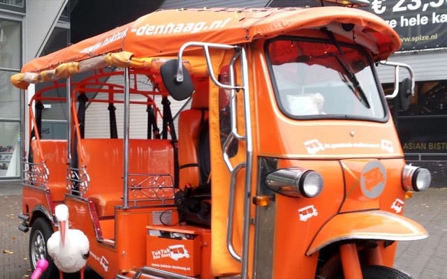 Oranje tuk tuk van Tuk Tuk Den Haag met een ooievaar ervoor, het symbool van Den Haag